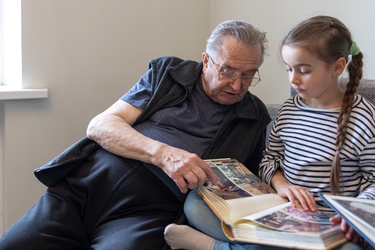 Starý otec ukazuje vnučke fotografie v rodinnom albume — odovzdávanie pamäti obce
